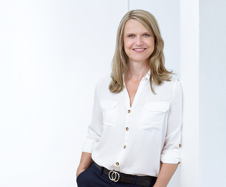 Portrait of DCZ team member Daniela Schilz smiling in white blouse in front of light background.