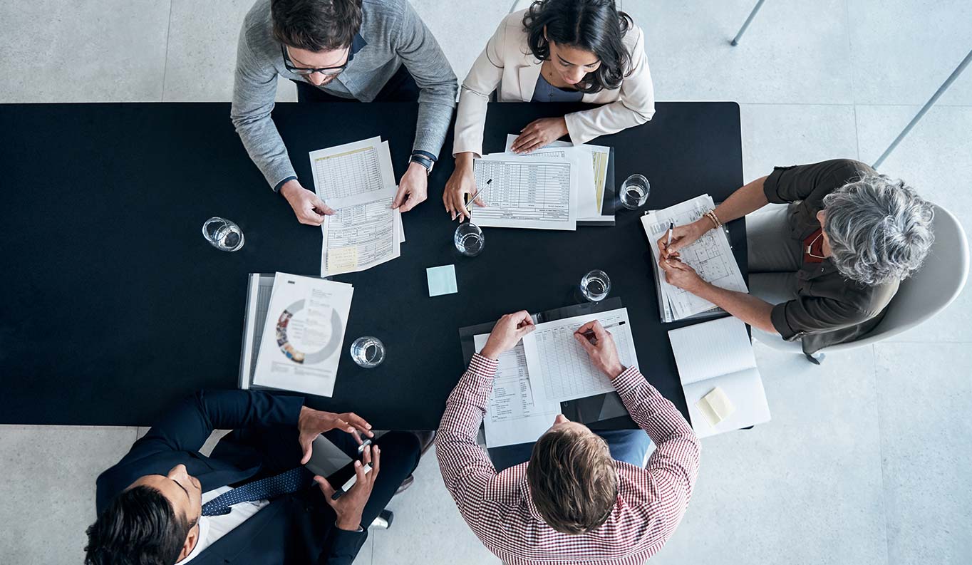 Scene of a team meeting at a table with spread out documents and water glasses from above