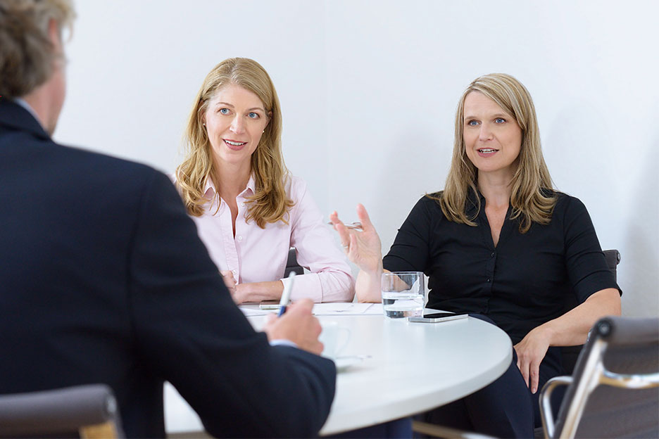 Daniela Schilz and Svea Ockenberg sitting at a table in conversation with a with a client.