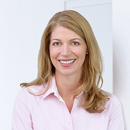 Portrait of DCZ team member Svea Ockenfeld smiling in pink blouse in front of light background.
