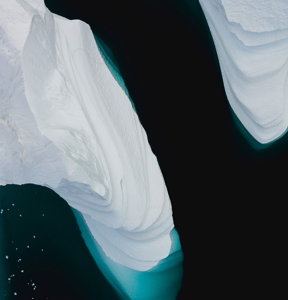 Part of a white iceberg from above, surrounded by dark greenish water.